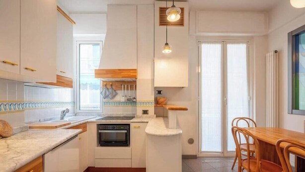 Ett modernt kök med vita skåp, en inbyggd ugn och en matplats med trästolar.