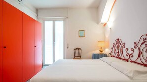 Ett hotellrum med en säng, en röd garderob, ett litet bord med en lampa och ett fönster med persienner.