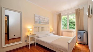 Een slaapkamer met een bed, nachtlampjes, een radiator, een raam met gordijnen en een wandheater.