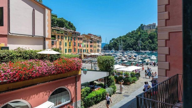 Vista di una marina con barche, un'area vivace di caffè all'aperto e edifici colorati sullo sfondo.