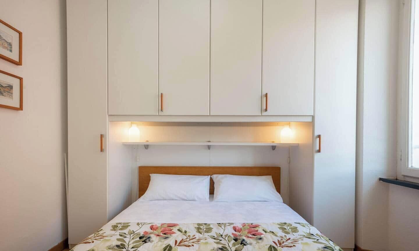 Une chambre à coucher avec un lit, des placards blancs au-dessus et deux lampes fixées au mur.