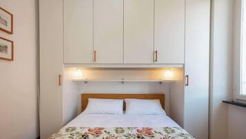 Une chambre à coucher avec un lit, des placards blancs au-dessus et deux lampes fixées au mur.