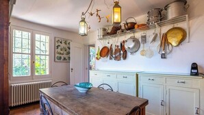 Een keuken met een houten tafel, hangende pannen en een radiator.