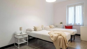 A bedroom with two beds, a bedside table with a lamp, a red chair, and a window with curtains. - Cocca by PortofinoVip [2 BRs-AC-Seaview] (Portofino)