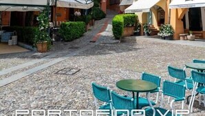 A cobblestone courtyard with outdoor seating, surrounded by colorful buildings with shutters and a bell tower in the background. - From I Gemelli Loft by PortofinoVip [AC-Shuttle] (Portofino)