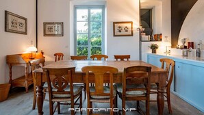 Ein Esszimmer mit Holztisch und -stühlen, einem Fenster mit Blick auf Grünflächen und gerahmten Bildern an den Wänden.
