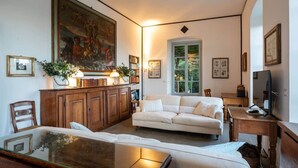 Ein Wohnzimmer mit einem weißen Sofa, einem Holzschrank, einem großen Gemälde und einem Bücherregal.
