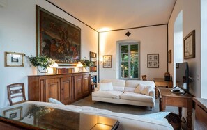 A living room with a white sofa, a wooden cabinet, a large painting, and a bookshelf.
