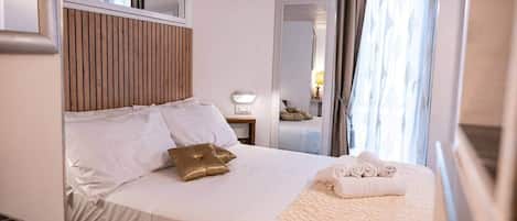 Une chambre d’hôtel avec un lit, une table de chevet, un miroir et une fenêtre avec des rideaux.