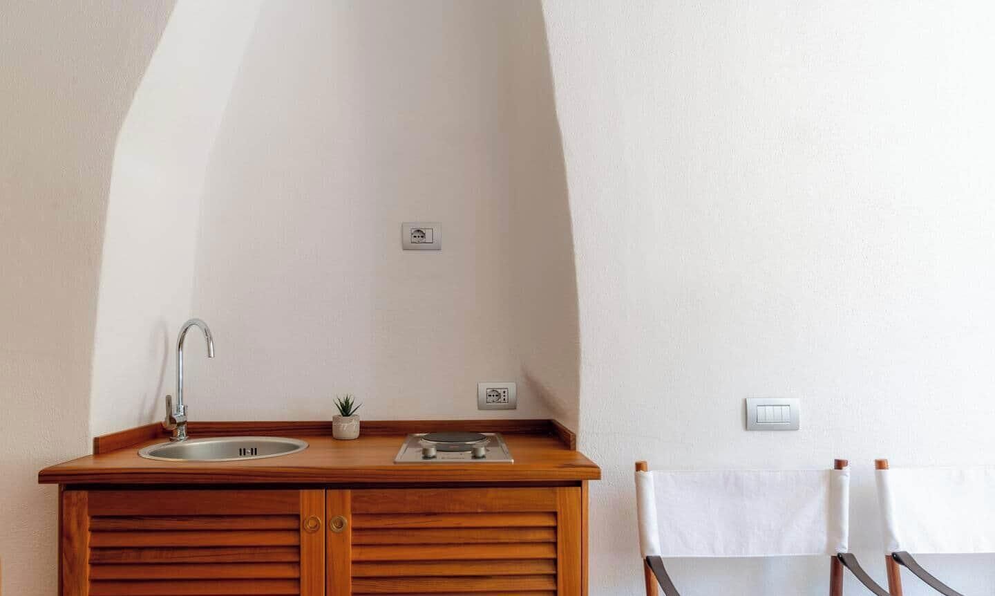 Una kitchenette pequeña con lavabo, estufa y una silla con toalla.