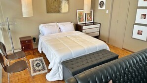 A bedroom with a bed, bedside tables, a dresser, a chair, a bench, and artwork on the walls. - 0516B (São Paulo)