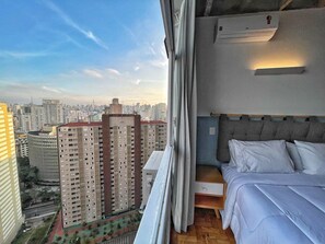 A bedroom with a city view, a bed, a nightstand, and an air conditioning unit. - 2101B (São Paulo)