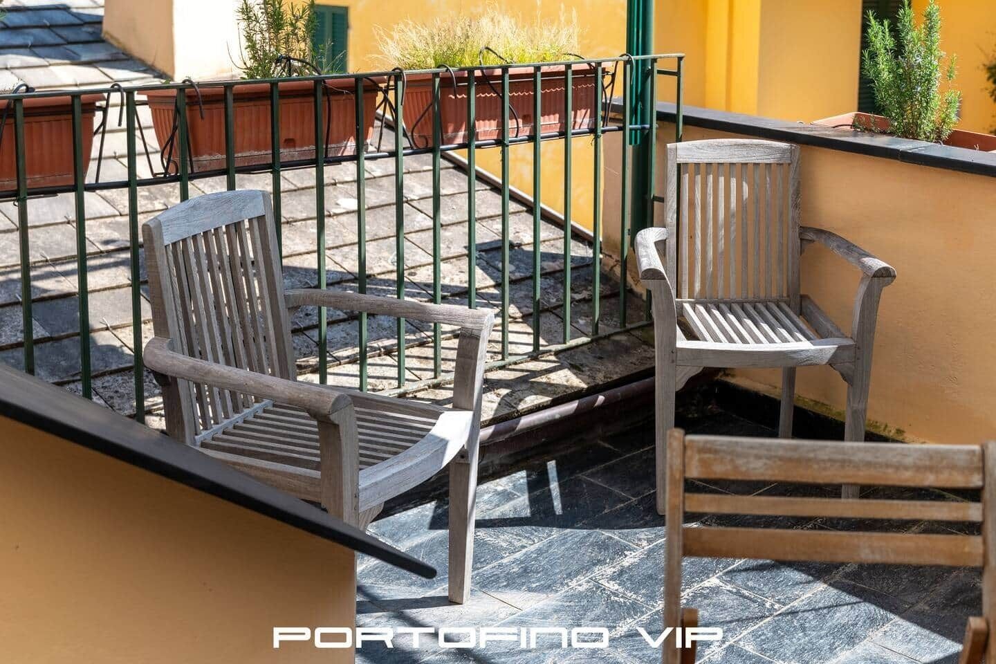 Un balcon avec deux chaises en bois, une rambarde en métal et des plantes en pot.