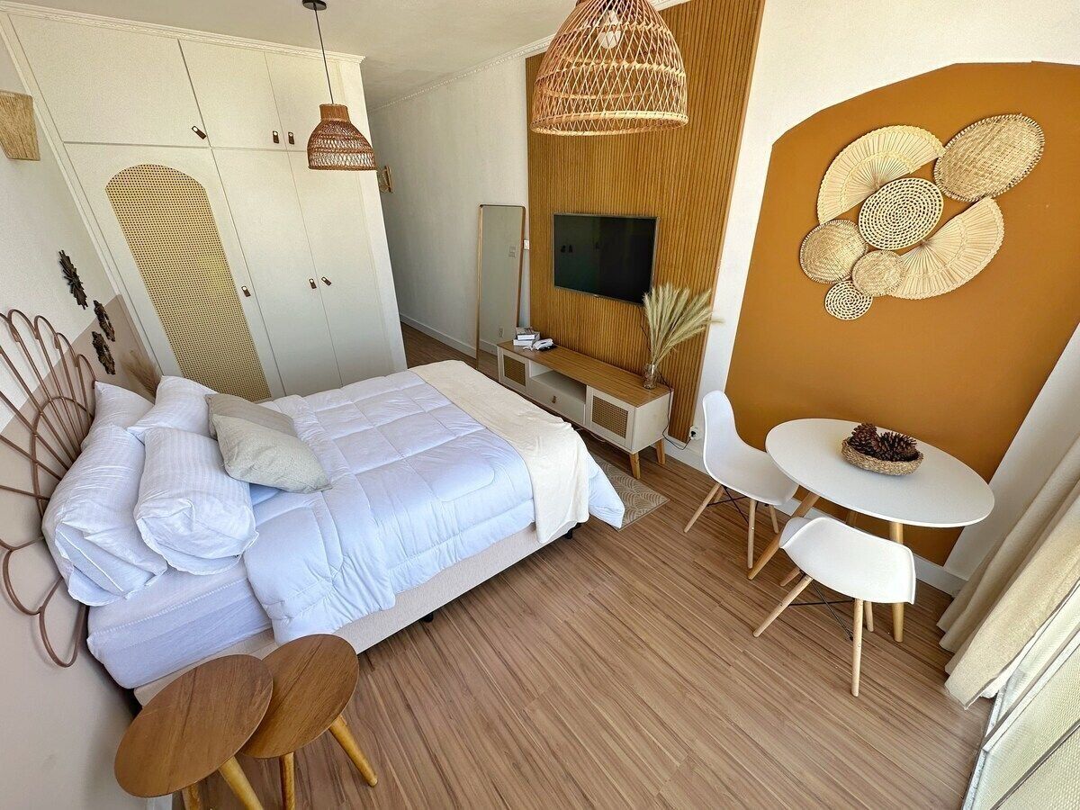 A modern bedroom with a bed, bedside tables, a TV, and a dining area with chairs and a table.