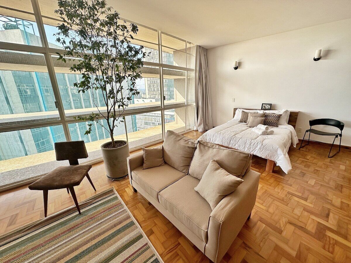 Quarto de hotel moderno com uma janela grande, um sofá, uma cadeira e uma cama.