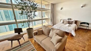 Quarto de hotel moderno com uma janela grande, um sofá, uma cadeira e uma cama.