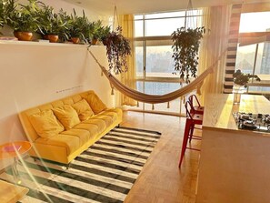 A living room with a yellow sofa, a striped rug, a hammock, and potted plants. - 0285F (São Paulo)