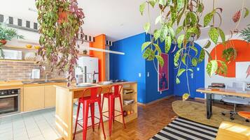 A modern kitchen with a hanging plant, red bar stools, and a blue accent wall.