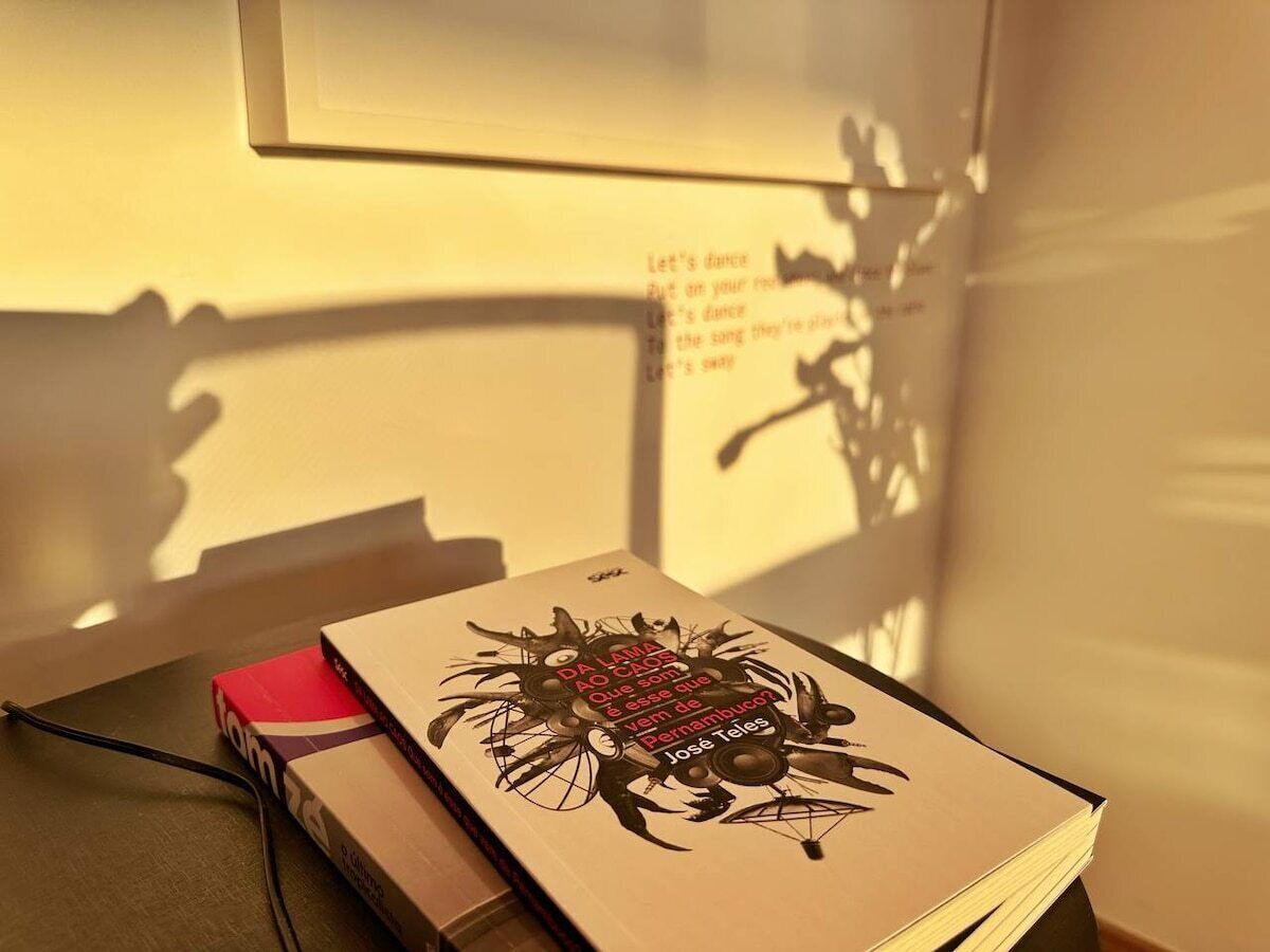 En bok med ett grafiskt omslag ligger på ett bord, och på väggen bakom syns skuggan av en växt.