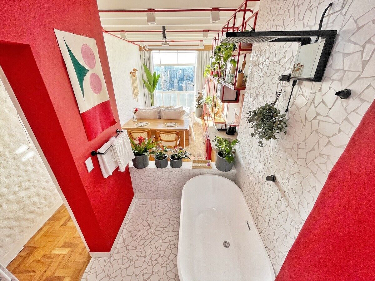 A modern bathroom with a freestanding bathtub, a red accent wall, and a city view.