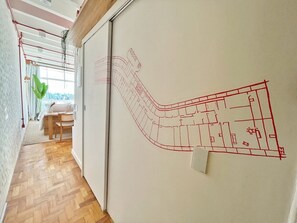 A room with a wooden floor, a white wall with a red line drawing, and a window with curtains. - 2701B (São Paulo)