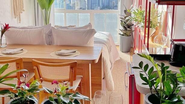 Sala moderna com vista para a cidade, área de jantar e cozinha com plantas em vasos.