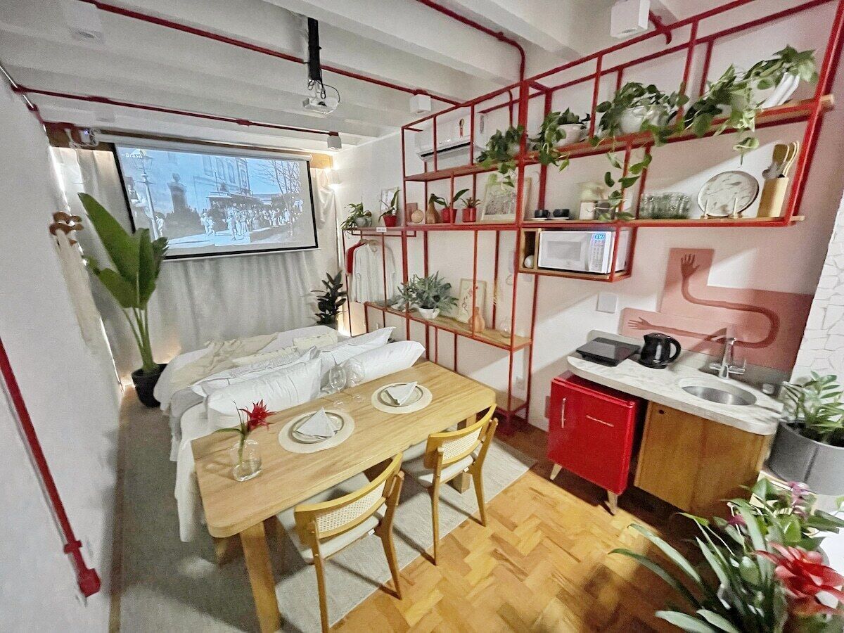 A compact living space with a dining area, kitchenette, and a TV displaying a cityscape.