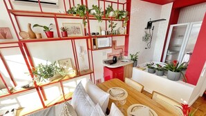Um interior moderno com área de jantar, cozinha e uma estante vermelha com plantas.