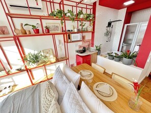 Ein modernes Interieur mit Essbereich, einer Küche und einer roten Regalwand mit Pflanzen.