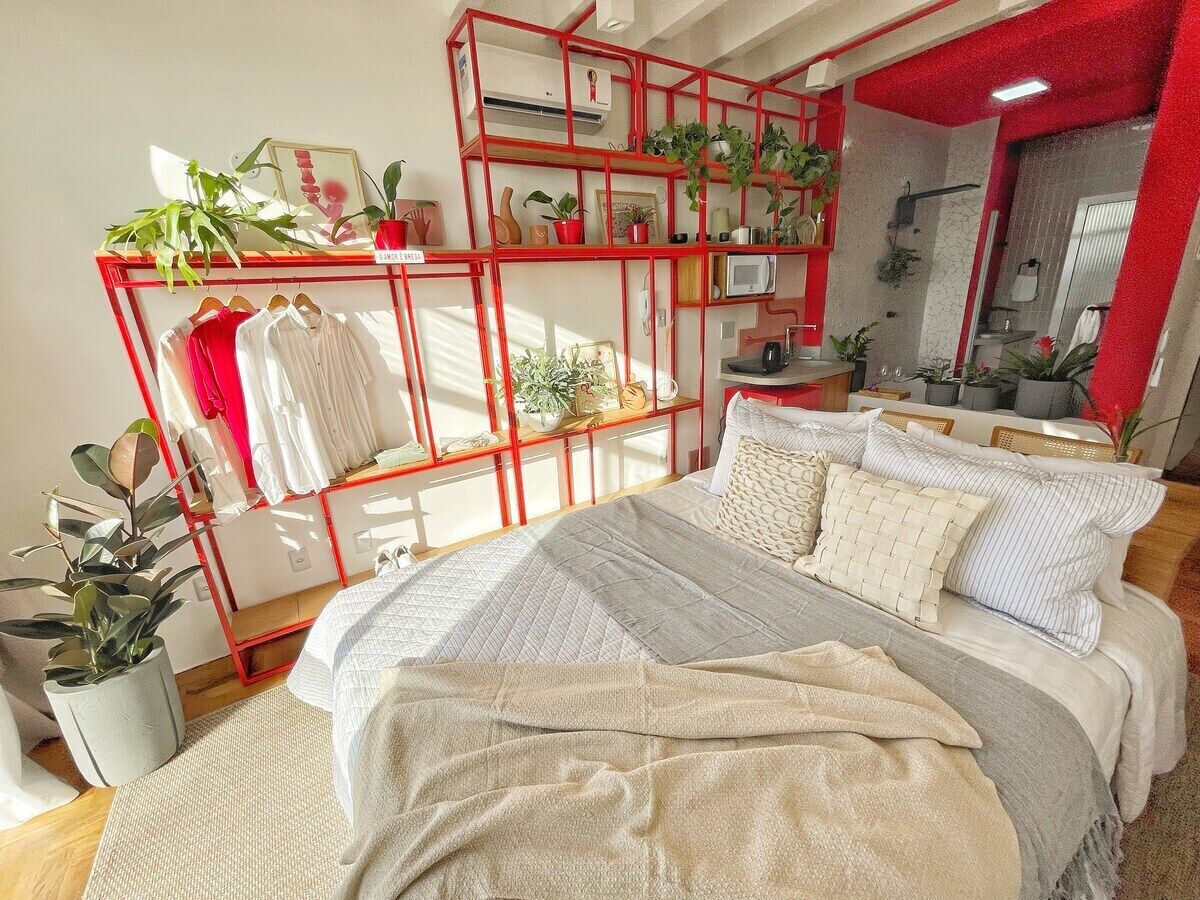 A bedroom with a bed, a red shelving unit, and potted plants.