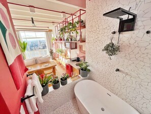 Ein modernes Badezimmer mit einer Badewanne, einer Dusche und einem an der Wand befestigten Regal mit Pflanzen.