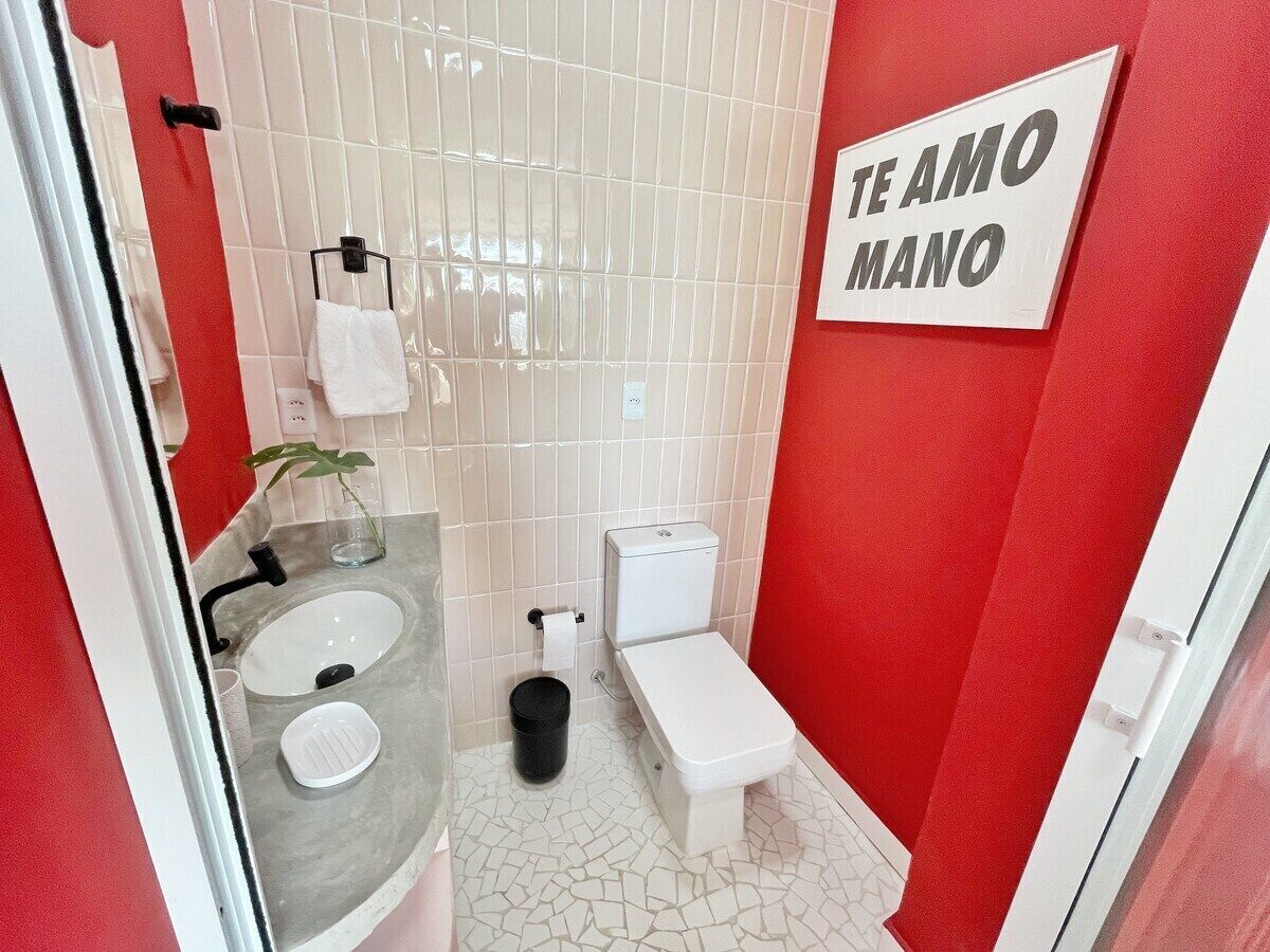 Une salle de bain avec un lavabo blanc, des toilettes et un mur rouge sur lequel est affiché un panneau avec l’inscription « TE AMO MANO ».