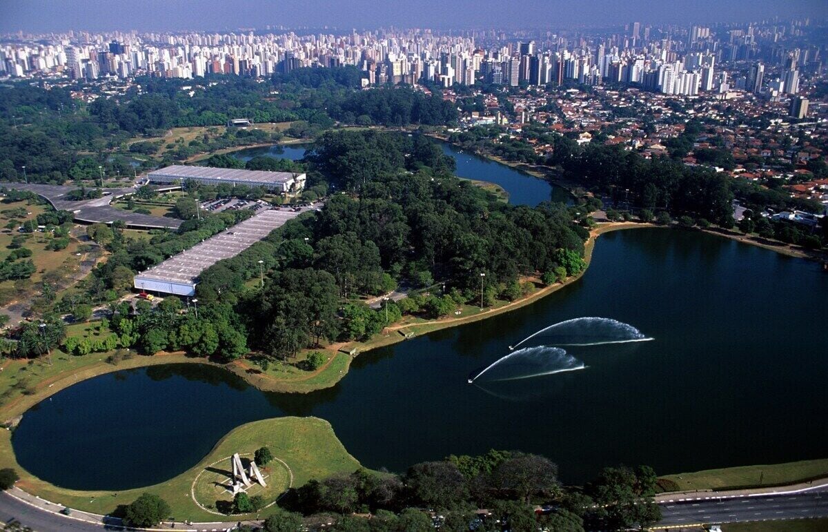An aerial view of a city with a large lake, surrounded by greenery and a few buildings.