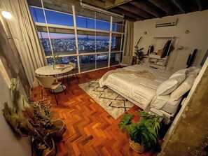 A bedroom with a large window, a bed, a round table, and a chair. - 2616B (São Paulo)