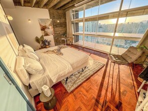 A bedroom with a large bed, a view of the city through floor-to-ceiling windows, and a wooden floor. - 2616B (São Paulo)