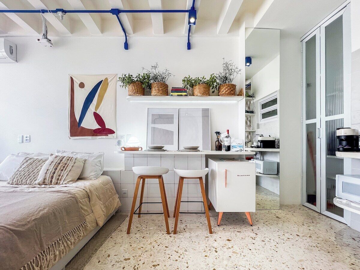 A modern bedroom with a bed, a desk, and a kitchenette.
