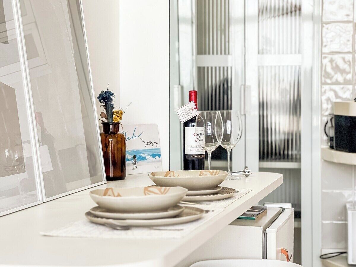 A modern kitchen with a white countertop, a wine bottle, glasses, and a decorative vase.