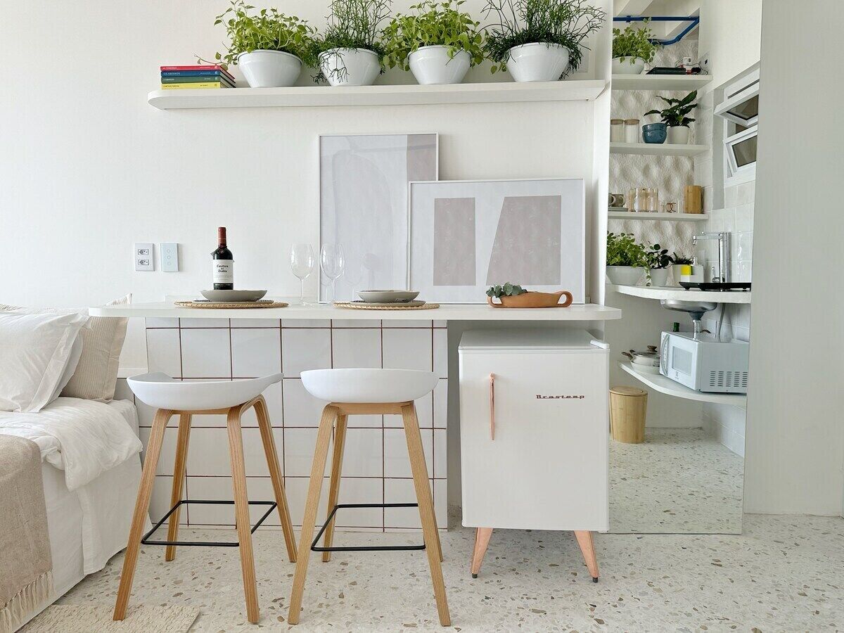 Eine moderne Küche mit weißer Arbeitsplatte, zwei weißen Barhocker, einem weißen Kühlschrank und einem weißen Esstisch.