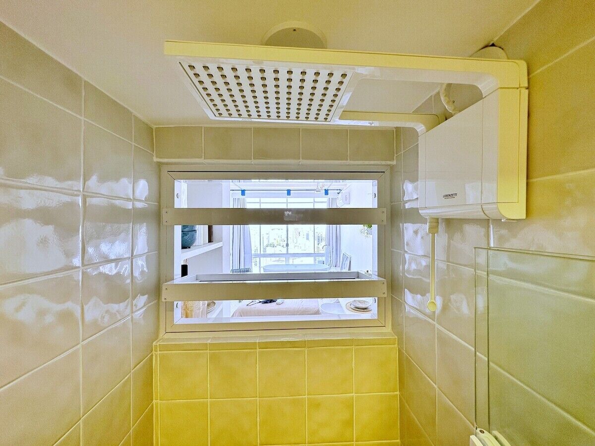 Une salle de bain avec des carreaux jaunes, une fenêtre et une bouche d’aération au plafond.