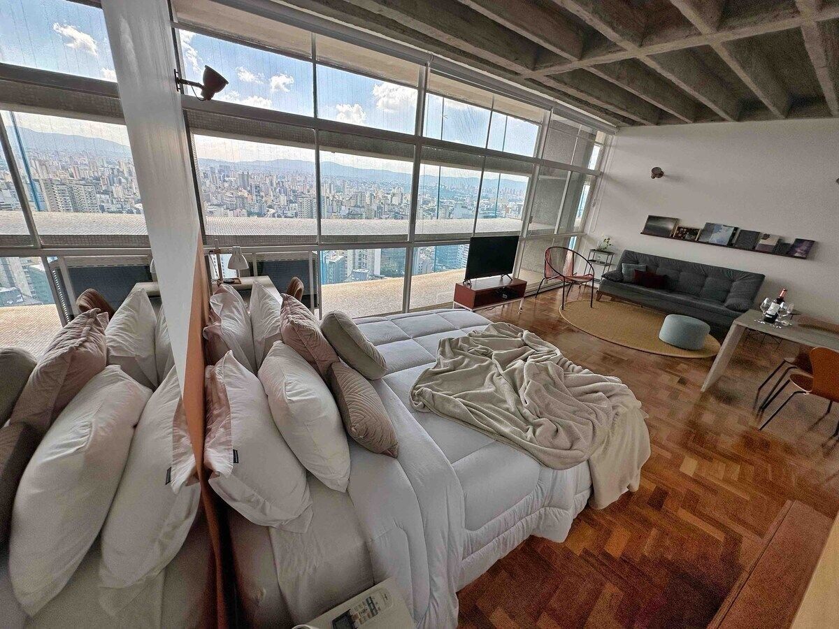 A bedroom with a large bed, multiple pillows, a TV, and a desk with a chair.