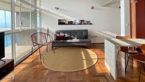 Ein moderner Wohnraum mit Fischgrätparkett, einem grauen Sofa, einem runden Teppich und einem Essbereich mit Tisch und Stühlen.