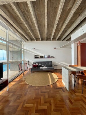 A modern living space with a herringbone wooden floor, a grey sofa, a round rug, and a dining area with a table and chairs. - 3017B (São Paulo)