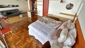 Ein modernes Schlafzimmer mit einem großen Bett, einem kleinen Schreibtisch, einer Couch und einem Essbereich.