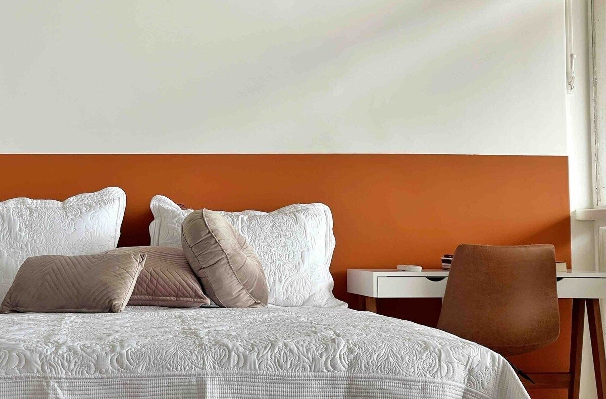 A hotel room with a bed, pillows, a chair, and a desk.