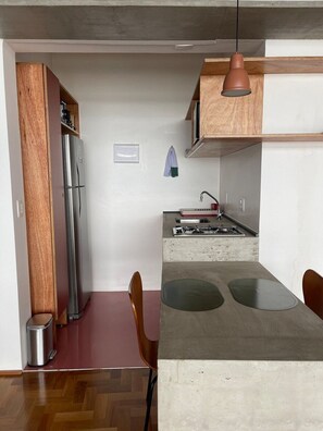 Een kleine keuken met een inbouwkoelkast, een gasfornuis en een eethoek met een tafel en stoelen.