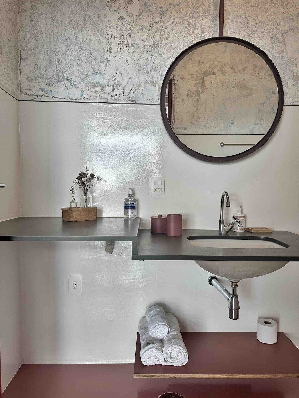 Une salle de bain avec un lavabo en verre, un miroir rond, un porte-serviettes avec des serviettes et des articles de toilette.