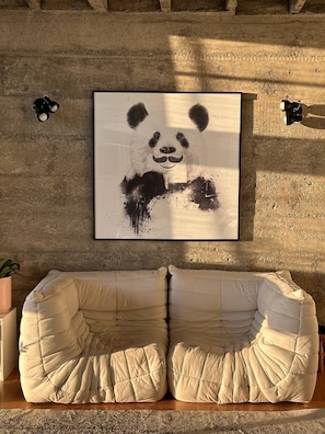 A framed artwork of a panda on a textured wall, a beige sofa, and two wall-mounted lamps. - 2717B (São Paulo)