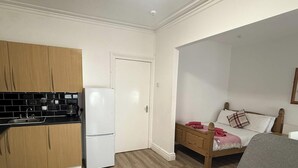 Una habitación pequeña con kitchenette, una cama y un sillón gris.