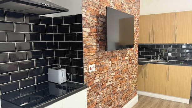 Una cocina con salpicadero de azulejos blanco y negro, pared con diseño de ladrillo, televisor de pantalla plana, armarios de madera y pileta de acero inoxidable.