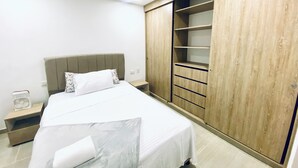 A bedroom with a bed, a nightstand, a wooden wardrobe, and a built-in shelving unit. - Beautiful fully equipped apartment (Ibagué)